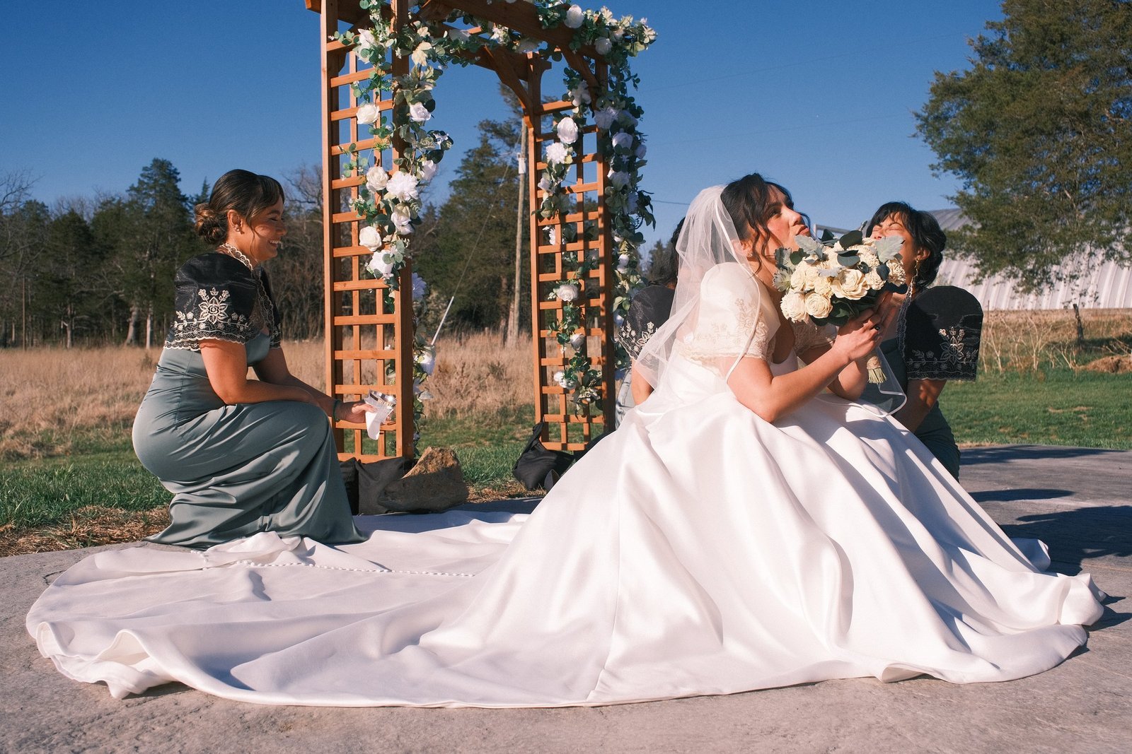 Bride seated with her gown spread beneath the floral arch in Luray, Virginia