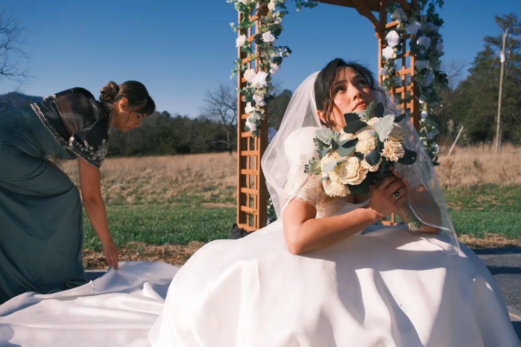 Bridesmaid arranging the bride’s train beside the floral arch