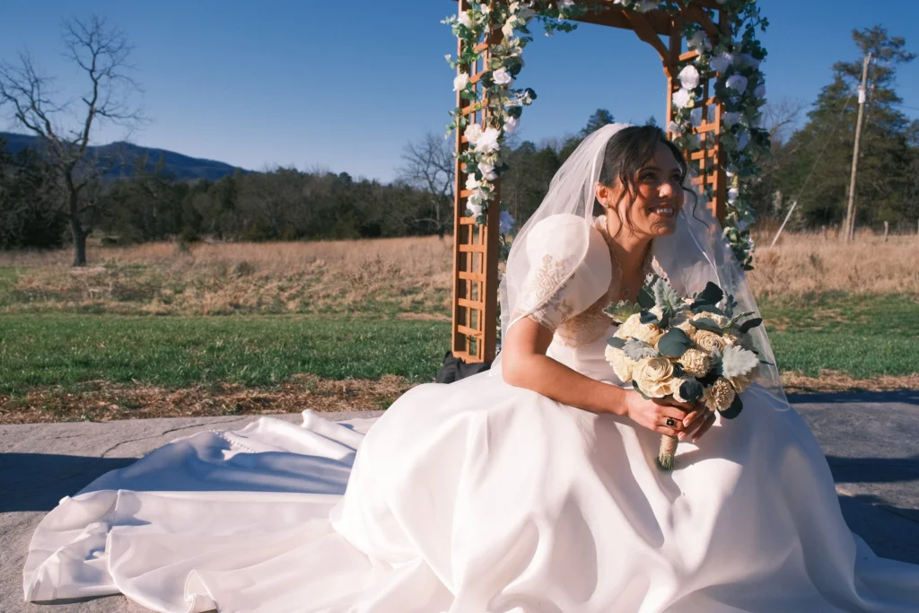 Bride smiling with her bouquet beneath the floral arch