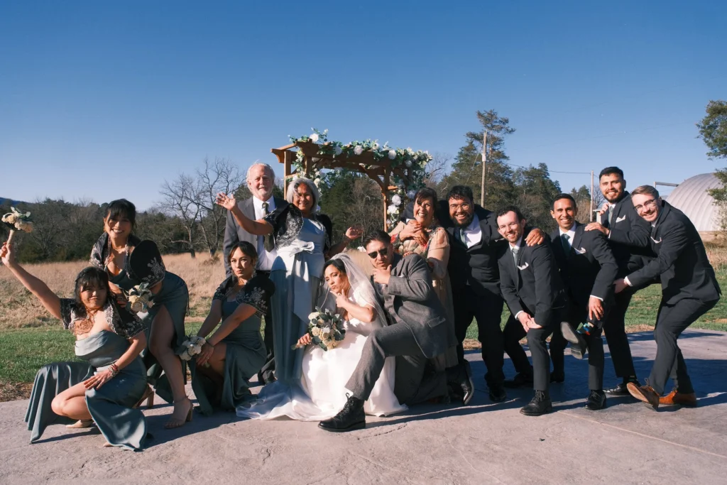 Wedding party posing playfully around the couple at the arch
